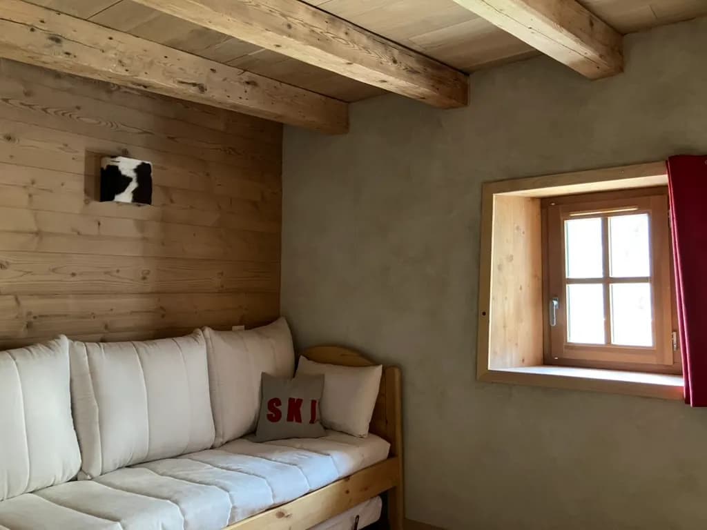 La banquette-lit sous la fenêtre à croisillons et son rideau rouge