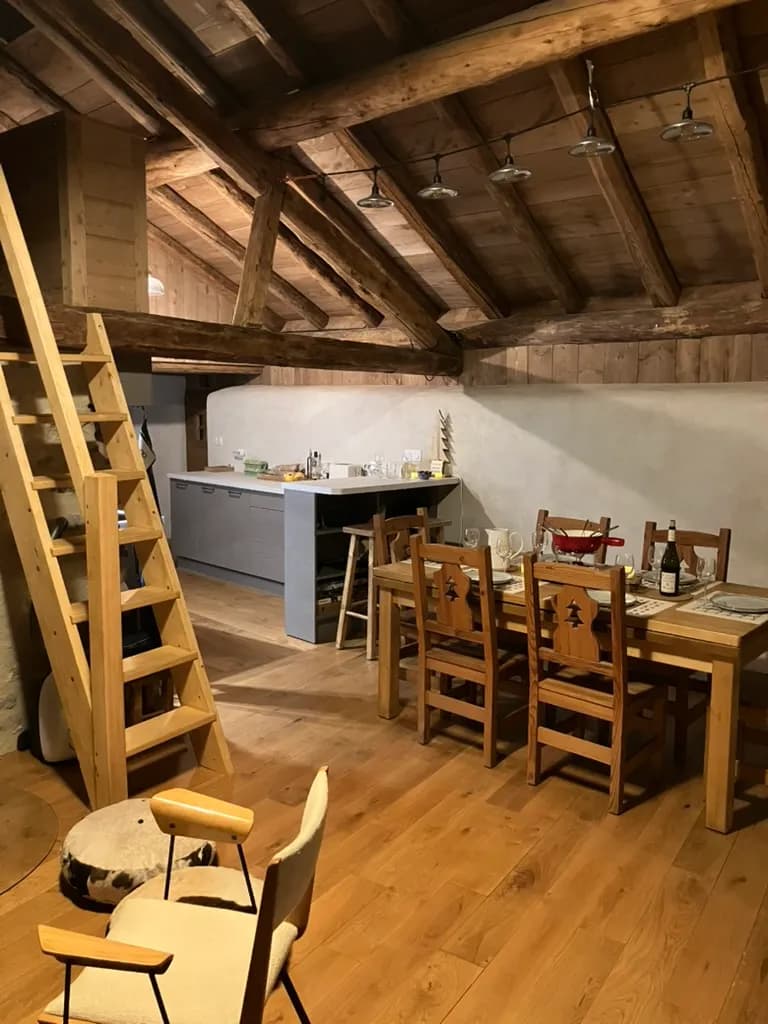 Poutres apparentes, table en bois et chaises autour d'un poêle dans le séjour