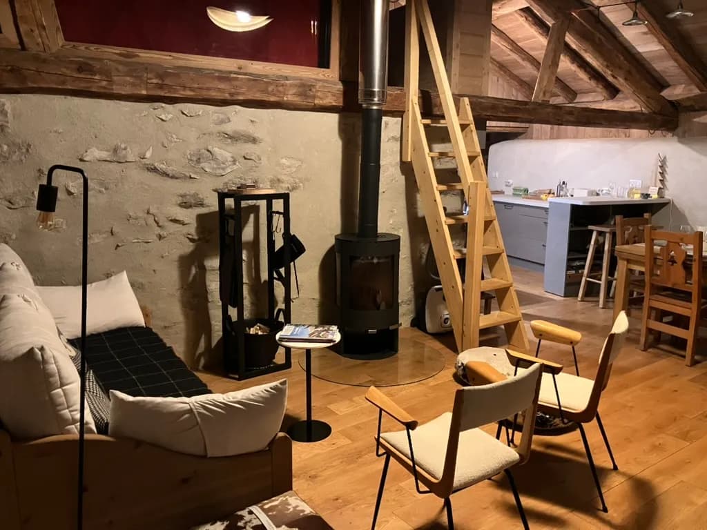 Séjour au mur de pierre avec canapé, poêle noir et cuisine ouverte