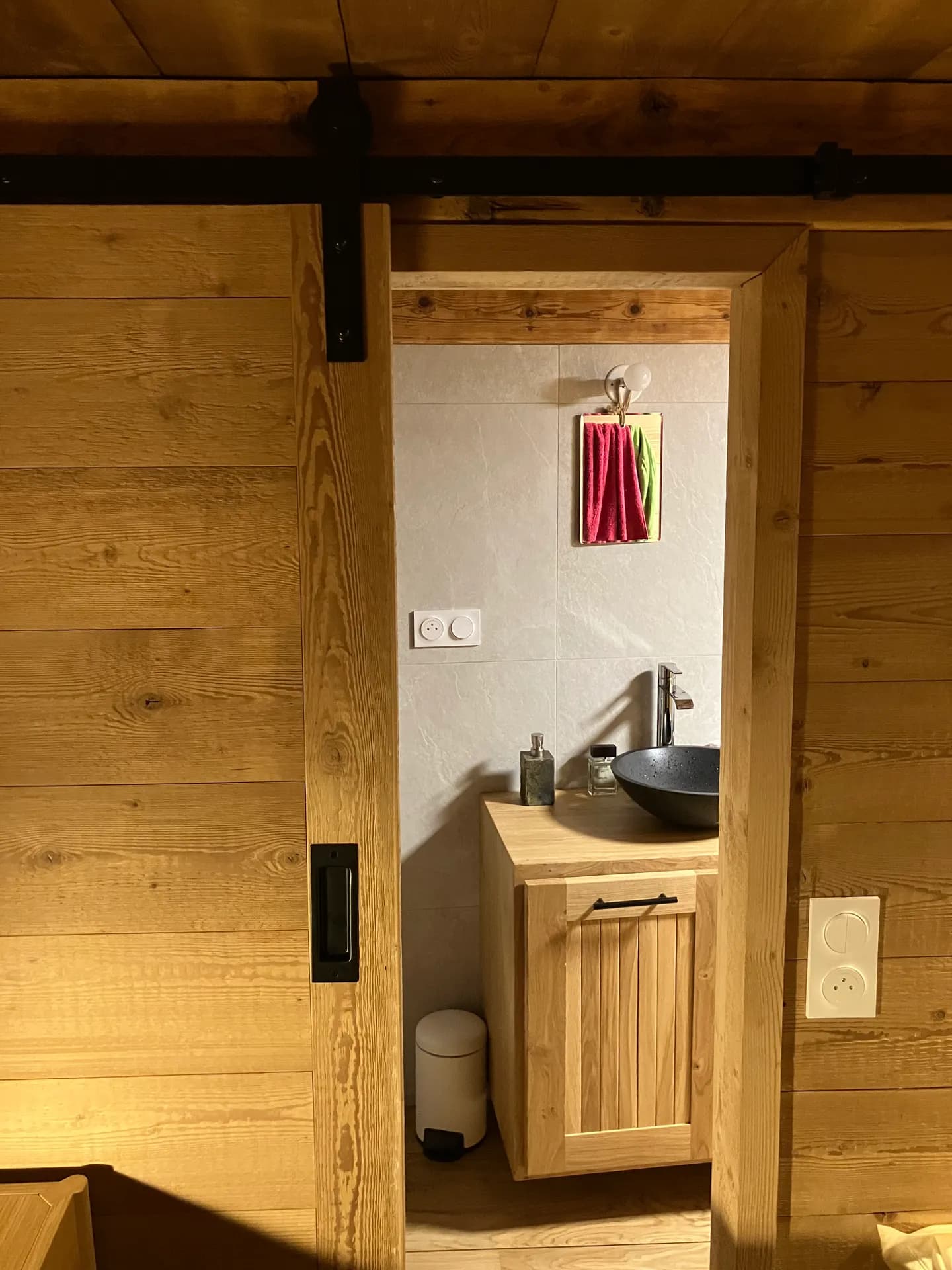 La salle d'eau de la suite vue de la chambre : vasque noire sur meuble chêne