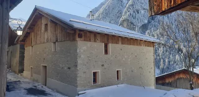 Chalet en pierre et bois sous la neige, fenêtres à volets rouges