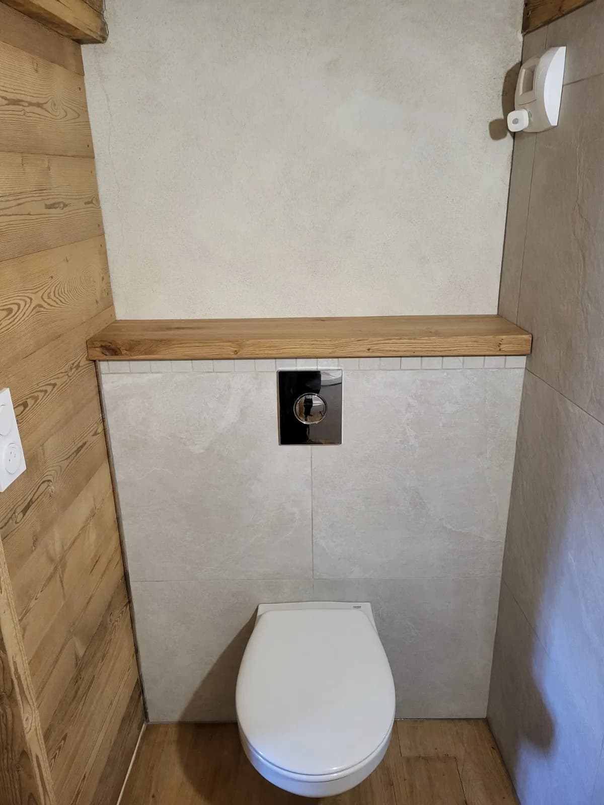 WC suspendu blanc avec réservoir intégré et bouton de chasse sur mur carrelé beige