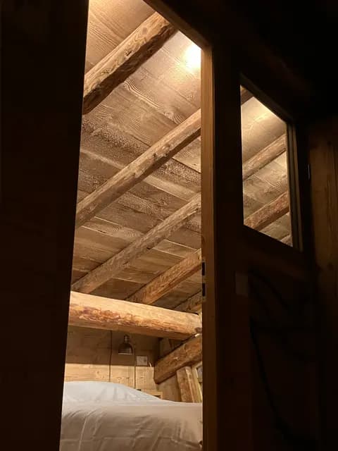 L'entrée de la chambre sous les combles, lit blanc sous les poutres anciennes