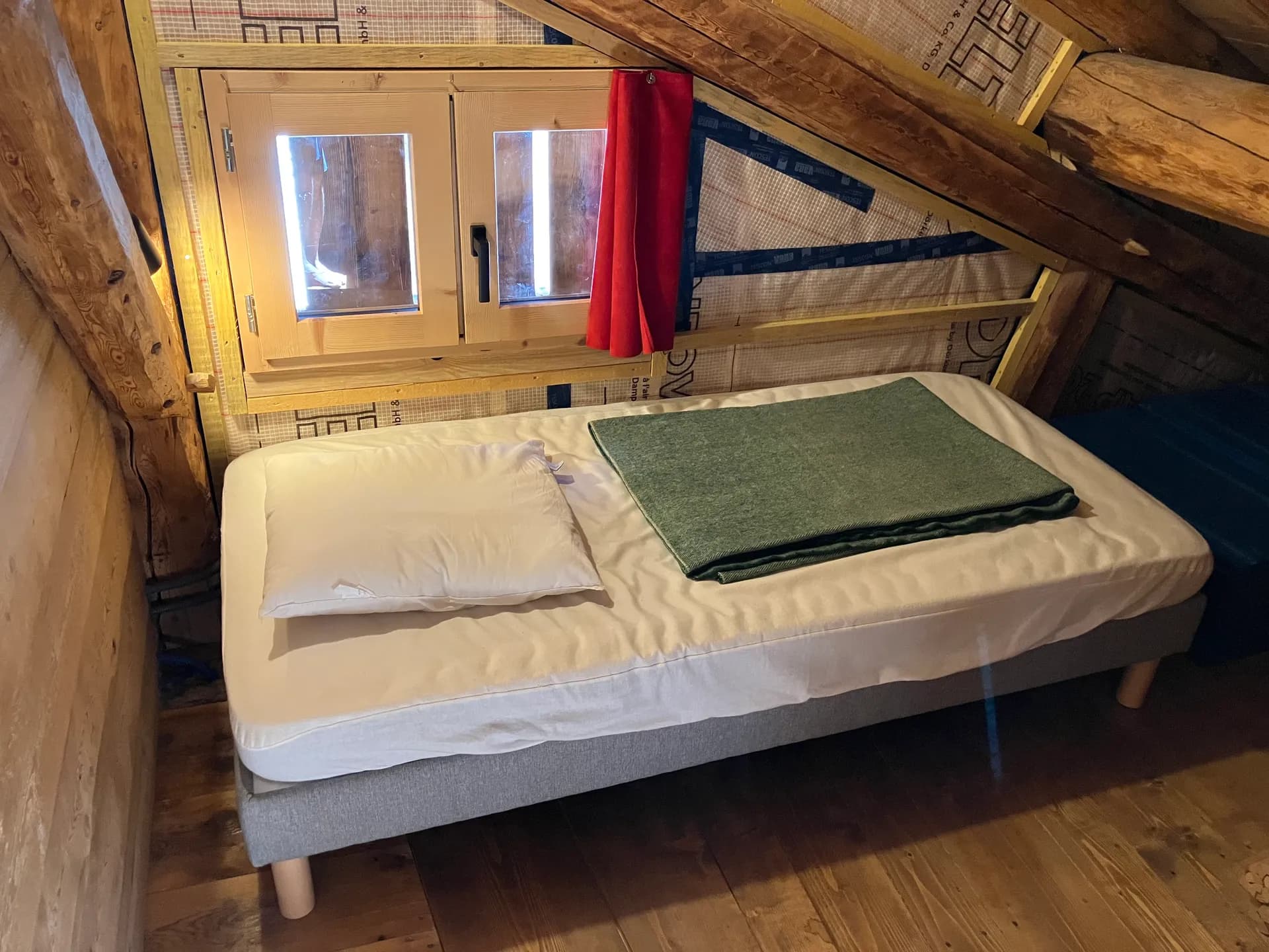 Lit double sous fenêtre avec couette verte dans chambre bois