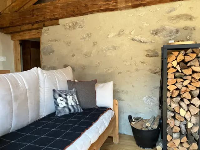 Canapé en tissu clair avec coussins et table basse en bois dans pièce aux murs en pierre apparente