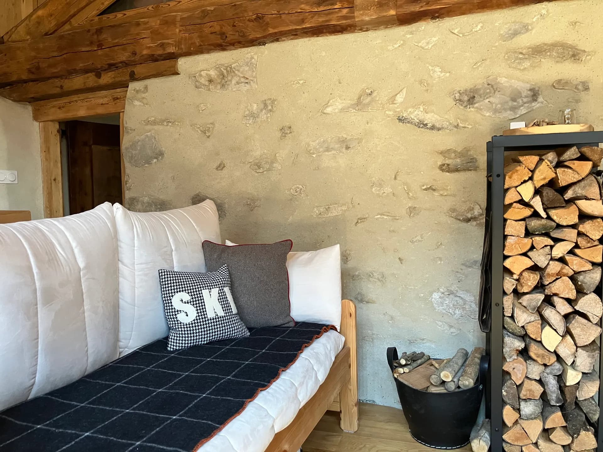 Canapé en tissu clair avec coussins et table basse en bois dans pièce aux murs en pierre apparente