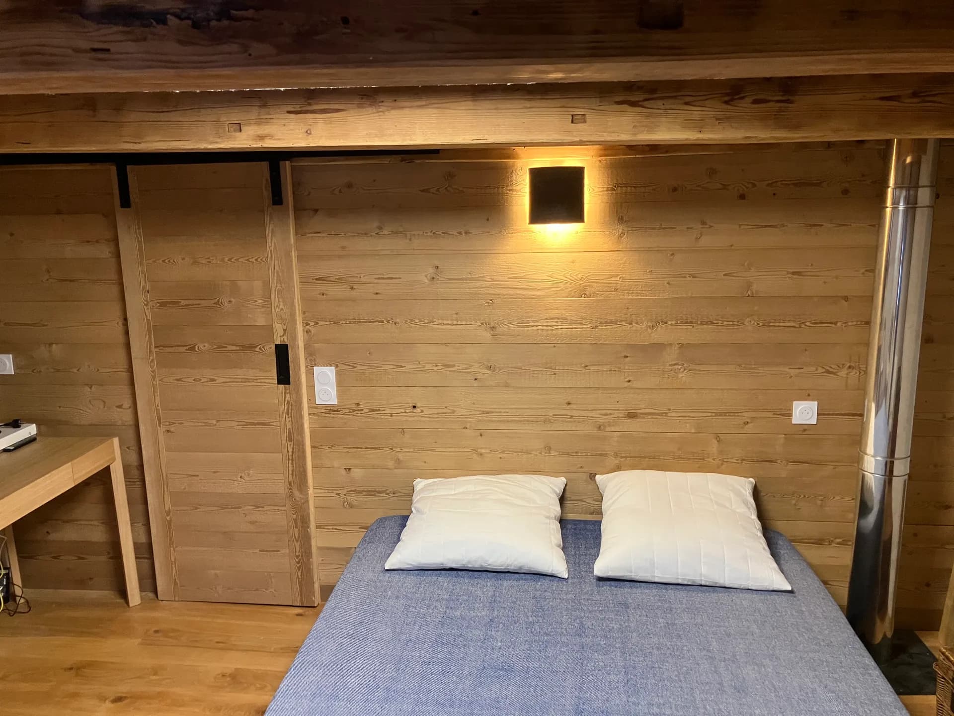 La tête de lit lambrissée de la suite, applique et porte coulissante en vieux bois