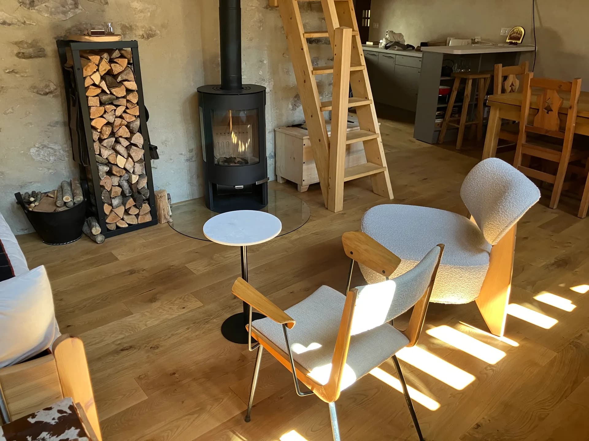 Coin repas avec table en bois et chaises, poêle à bois et cuisine équipée